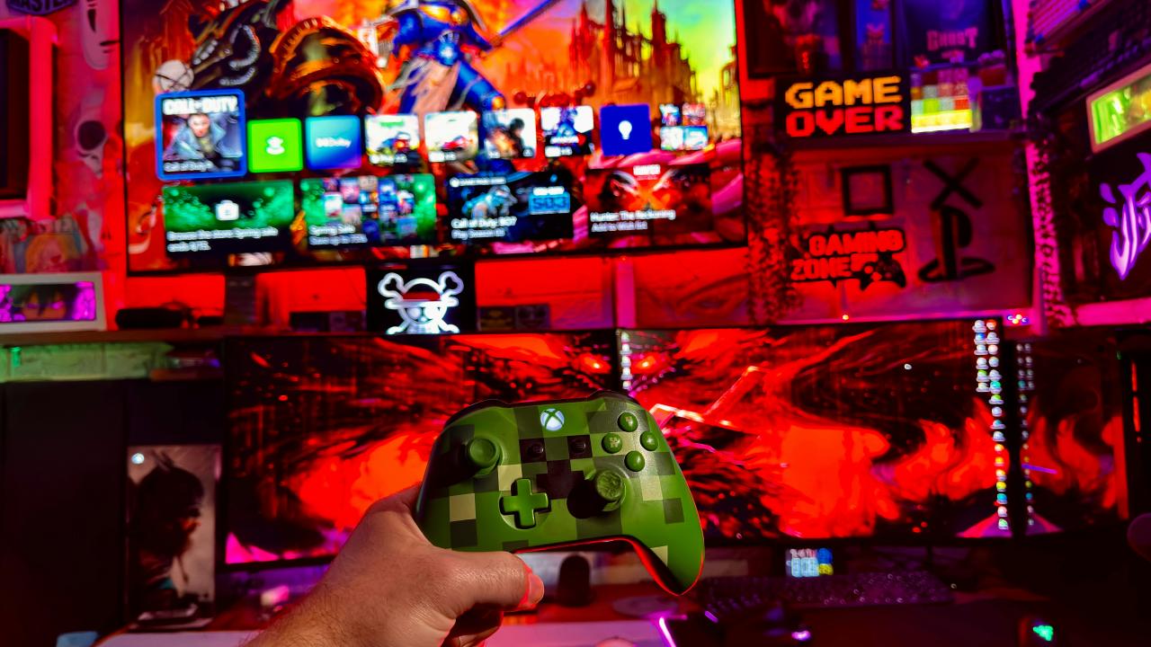 Person holding a video game controller in front of screens